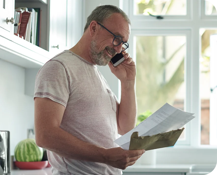 man smiling on phone looking at bills