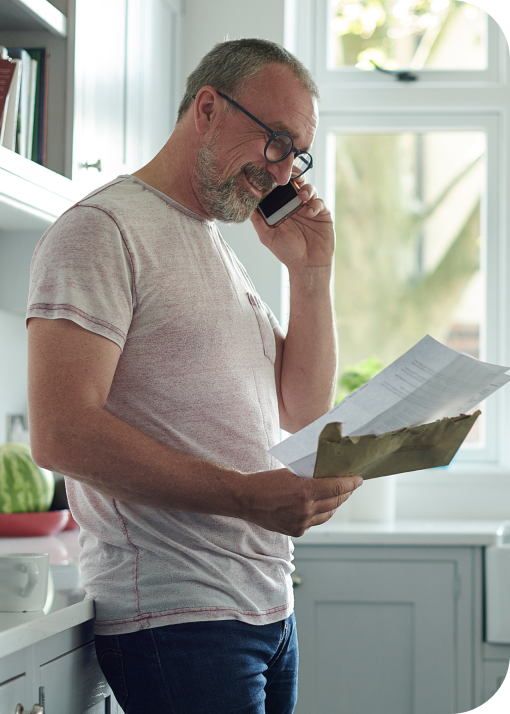 man standing in kitchen looking at paper bill